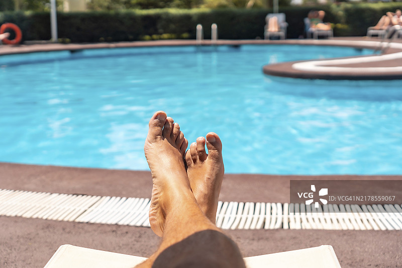 男人躺在躺椅上，俯瞰酒店度假村的泳池，享受日光浴图片素材