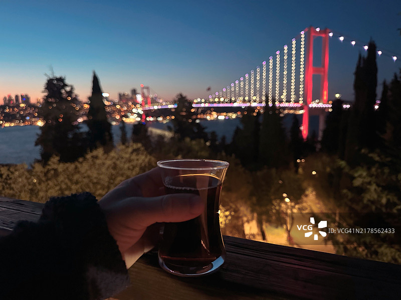 在夜晚的土耳其，手握饮料对着灯光璀璨的城市。图片素材