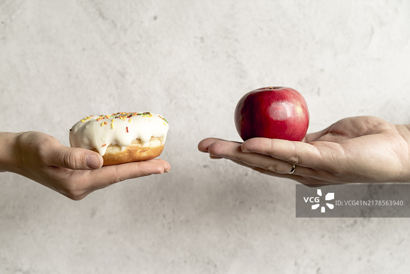 人手拿着甜甜圈苹果，前方是水泥背景图片素材