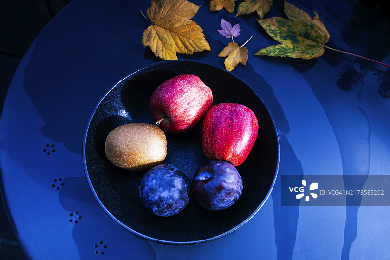 秋季黑碗里的苹果、猕猴桃和西梅图片素材