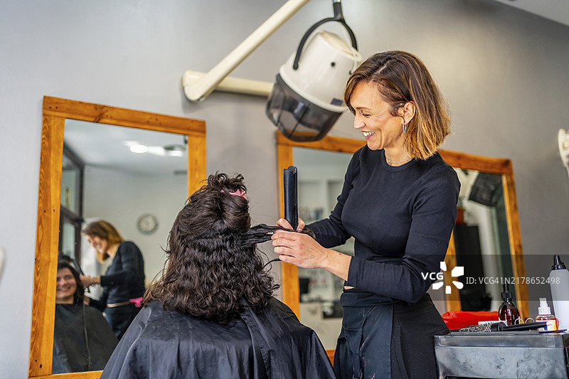 微笑发型师在沙龙为顾客卷发图片素材