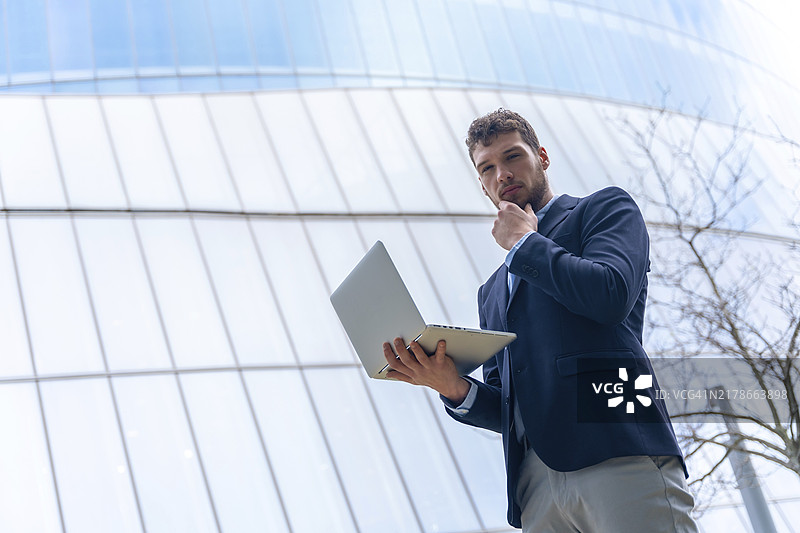 在玻璃建筑中使用电脑的年轻商人，金融概念图片素材