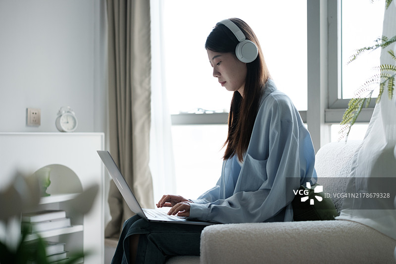 亚洲女人坐在沙发上使用笔记本电脑图片素材