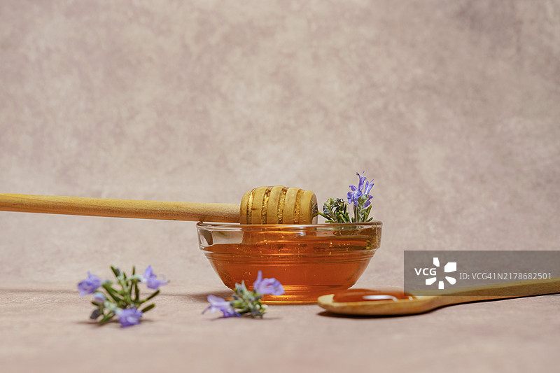 玻璃碗中的天然蜂蜜、木勺和新鲜迷迭香图片素材