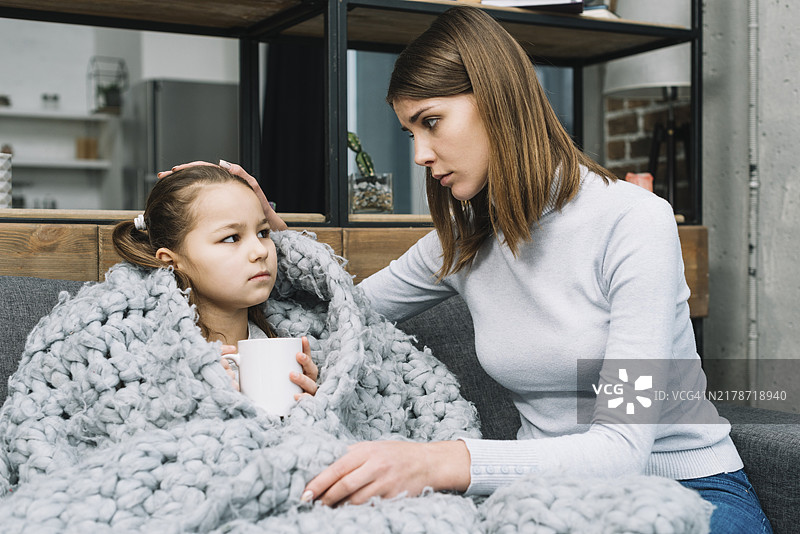 母亲照顾着发烧的女儿，女儿裹着灰色羊毛围巾图片素材