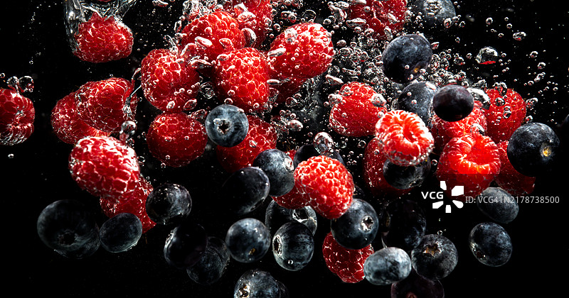 蓝莓和覆盆子溅入水中，带有气泡并沉入黑色背景中图片素材