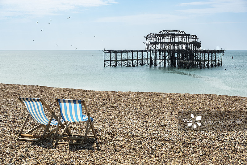 在布莱顿焚毁的西码头遗址前的海滩上的两把折叠椅，英国东萨塞克斯图片素材