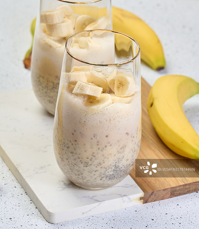 装有奇亚籽和酸奶的甜点杯，上面点缀着新鲜的香蕉片，放在白色桌子上。图片素材