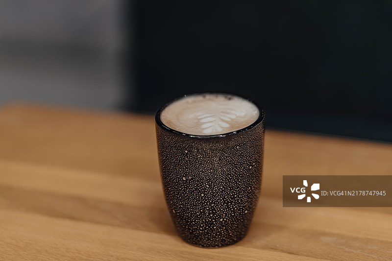 在泡沫中以精致的叶子图案庆祝咖啡艺术，盛在一个乡村风格的杯子里。图片素材