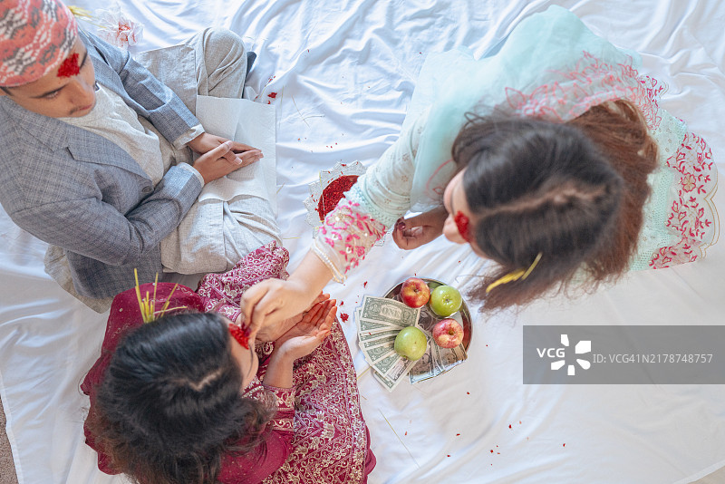 Dashain节（尼泊尔最重要的节日）——姐姐为妹妹点Tika——Dashami节——Dashain第10天——Dhakatopi帽子——俯视图片素材