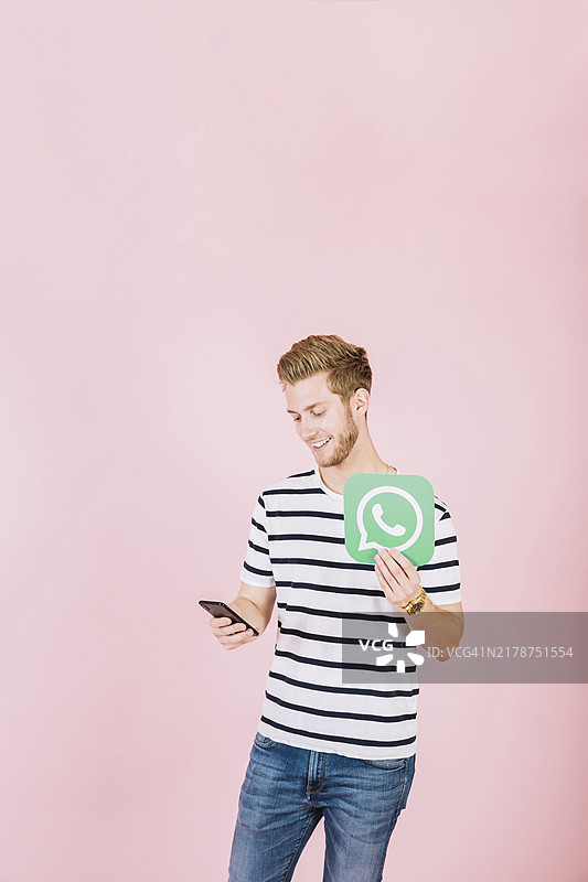使用带有WhatsApp图标的智能手机的快乐年轻人图片素材