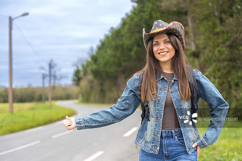 身穿牛仔服，头戴牛仔帽的女子在乡间小路上搭便车图片素材