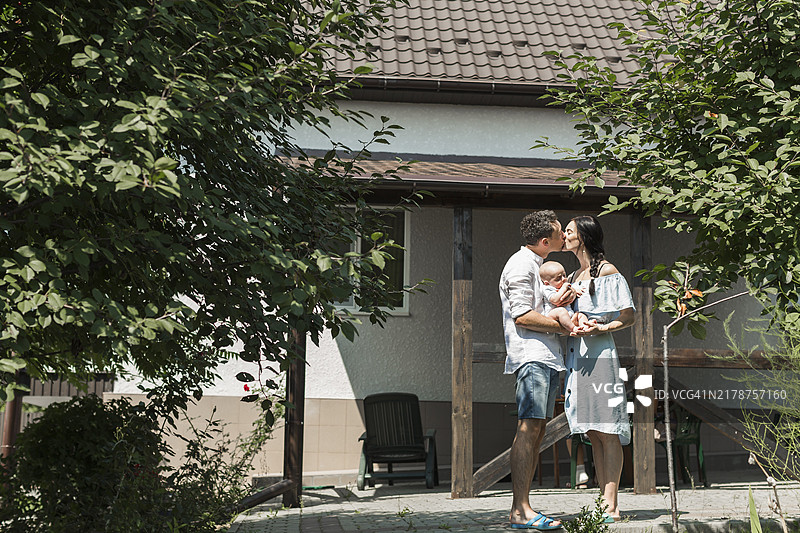 抱着孩子在房子前亲吻的情侣图片素材