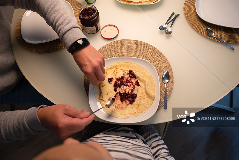 父亲为儿子在盘子里的薄煎饼上抹果酱图片素材