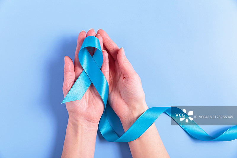 蓝色背景上女性手中的结直肠癌宣传丝带图片素材