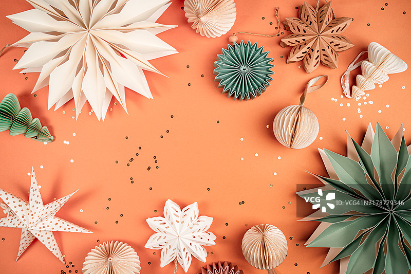 橙色背景上节日气氛的纸质雪花和圣诞树装饰品组合。圣诞快乐，新年快乐概念图案，带有复制空间。展示2024年度Pantone颜色 - 桃色。图片素材