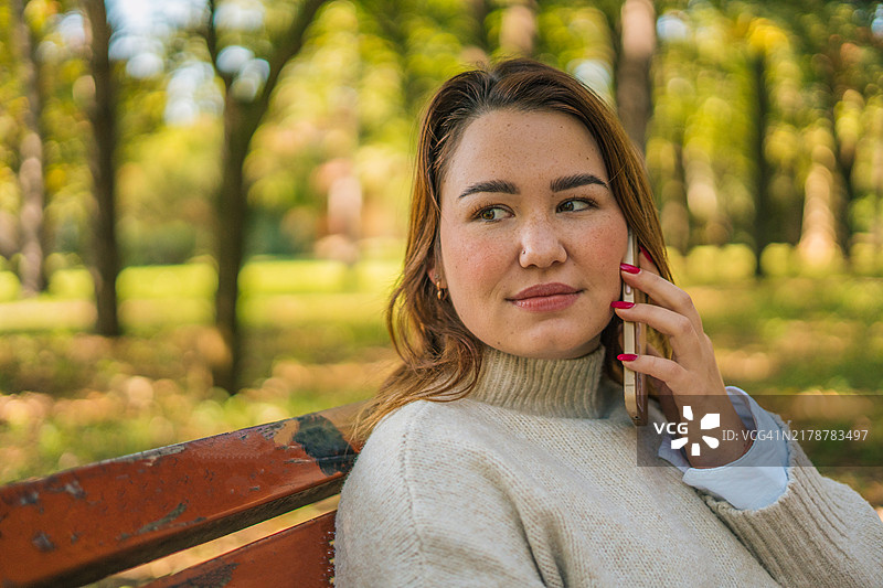 快乐的女士在户外长椅上打电话，拿着塑料杯。都市生活和交流概念图片素材