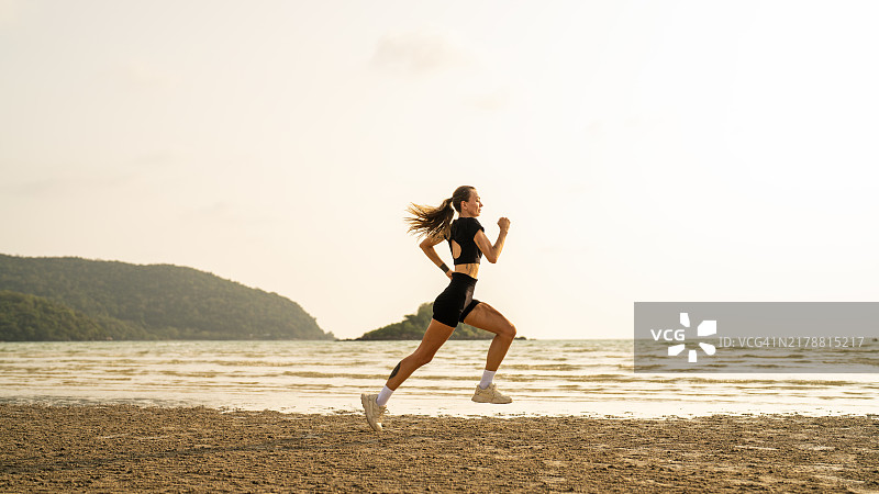 年轻女子在日出时分的海滩上跑步图片素材