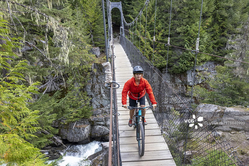 年轻女子骑山地自行车过悬索桥图片素材