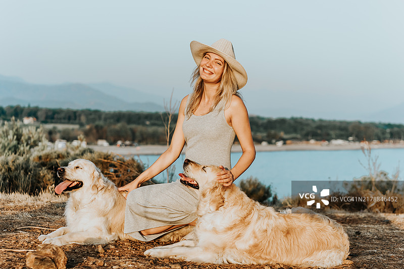 戴帽子的美丽女人与小狗在海边，日落光，宠物朋友概念图片素材