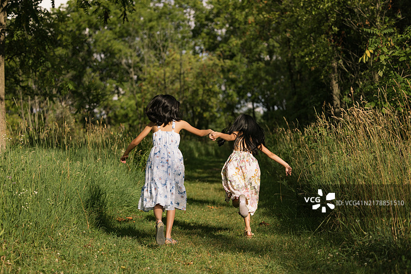 无忧无虑的女孩们在公园里奔跑的背影。图片素材