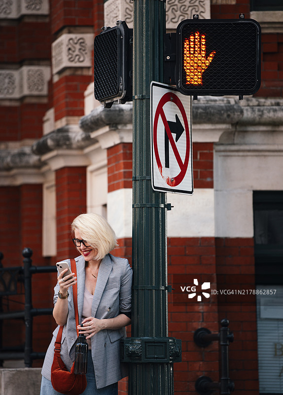 时尚金发女人在城市街角使用智能手机图片素材