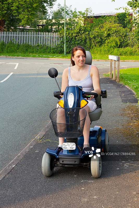 漂亮的少女在夏日的阳光下骑着残疾人电动滑板车，享受着这辆滑板车带给她的独立出行的自由，尽管她有残疾。图片素材