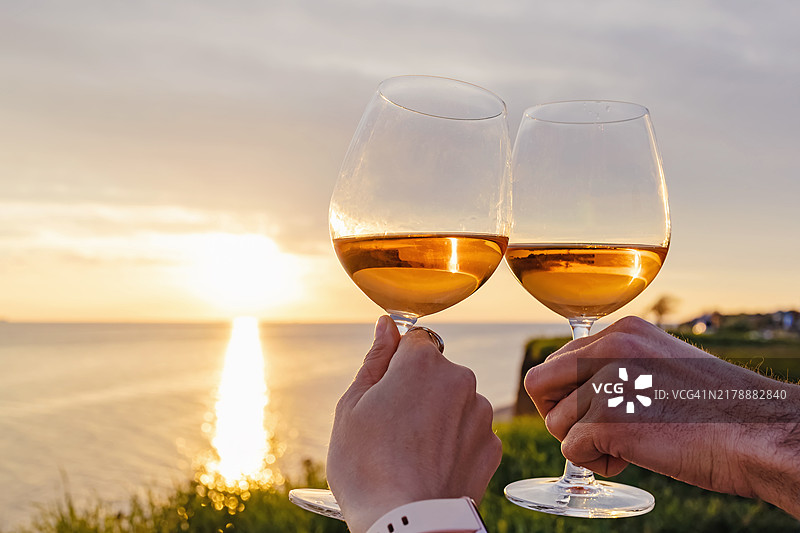 情侣在日落时分对着海面举杯祝酒的手部特写图片素材