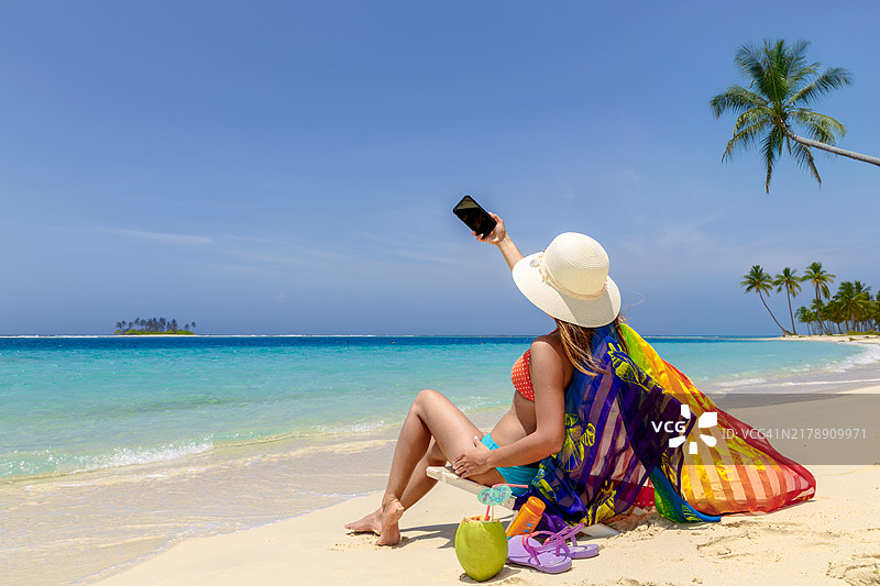 在白色沙滩热带海滩上享受日光浴并自拍的可爱西班牙裔年轻女人图片素材