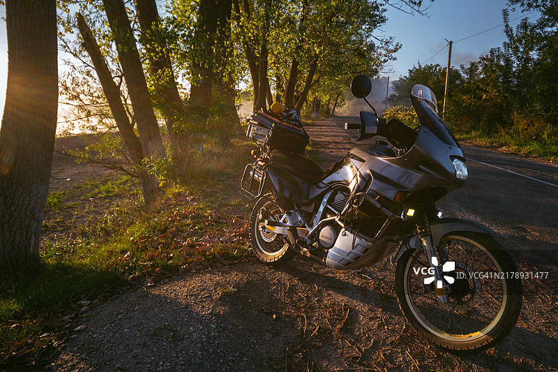 乌克兰赫梅利尼茨基，2023年9月10日：本田Transalp PD06 xl600摩托车，停在路边的旅游摩托车，可欣赏树木和日落景色，秋日温暖的黄色图片素材