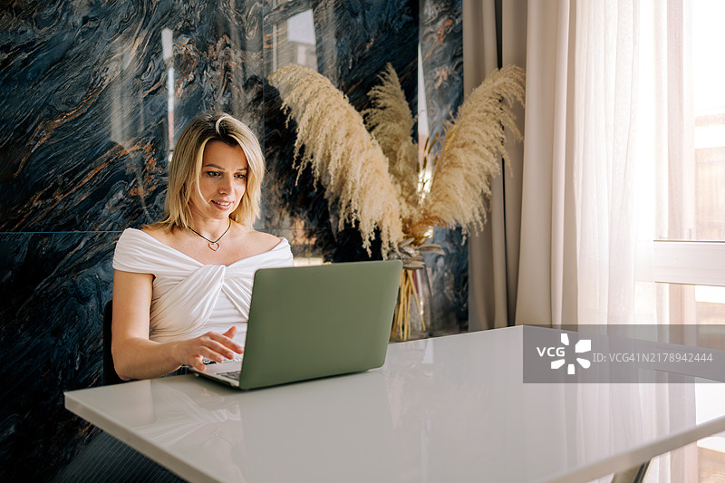 中年女性在家中使用笔记本电脑工作。自由职业，远程工作图片素材