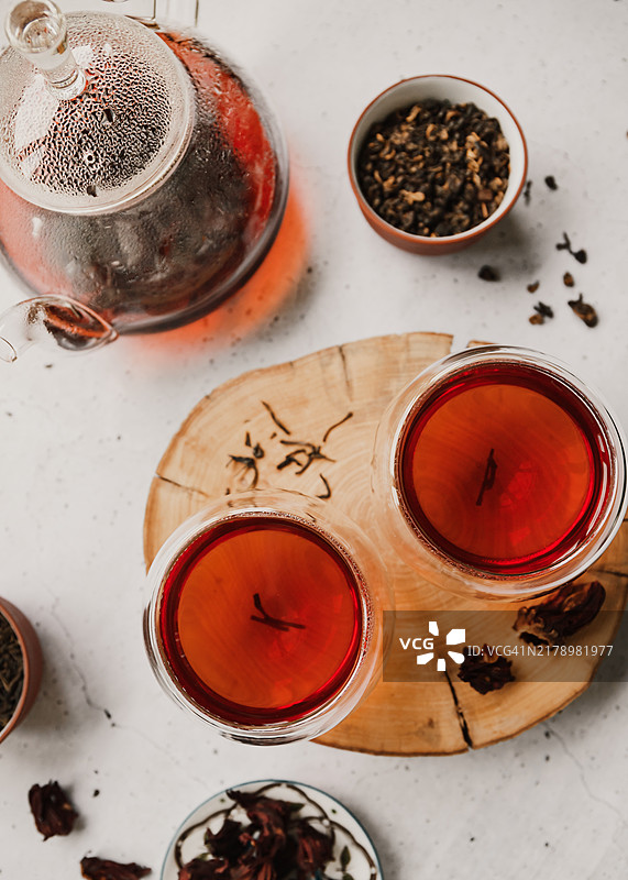 不同种类的茶：红茶、绿茶和洛神花茶，摆放在白色桌子上，旁边有茶壶和玻璃杯。图片素材