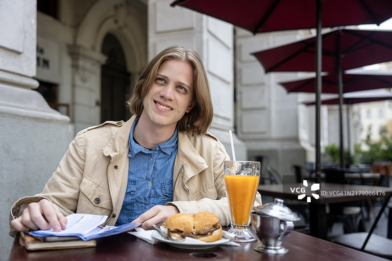 年轻男子在利马圣马丁广场的咖啡店享用牛肉三明治和橙汁。图片素材