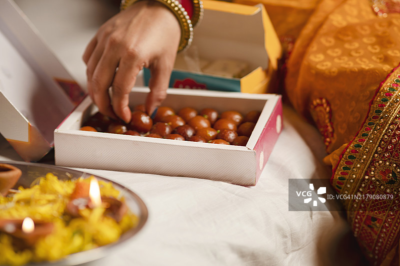 穿着纱丽的传统印度女性正在庆祝排灯节，手中拿着油灯和甜点。图片素材