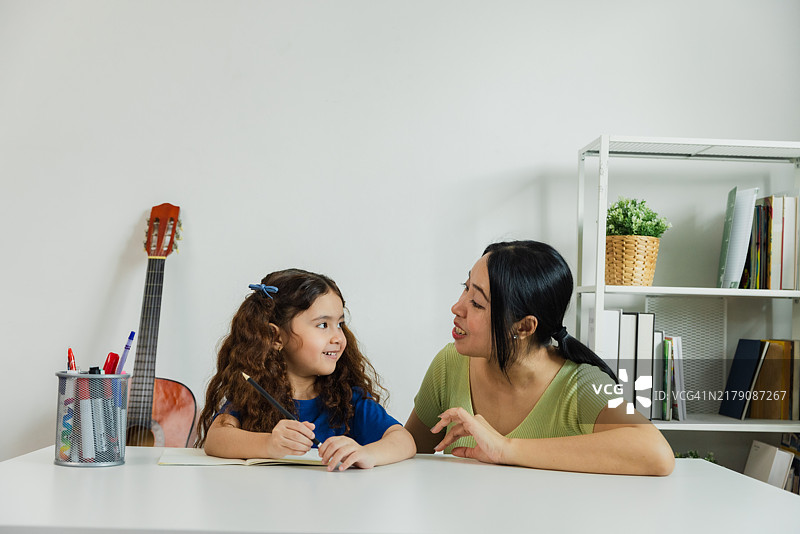 母亲在舒适的学习区帮助女儿做作业，学习区内有吉他和书架。图片素材