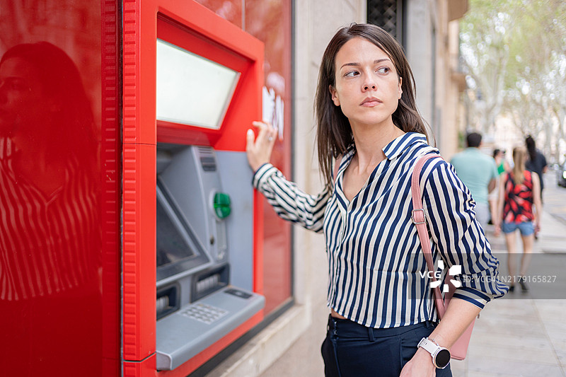 年轻女子站在ATM机前输入密码，专注于在西班牙马略卡岛帕尔马的交易安全图片素材