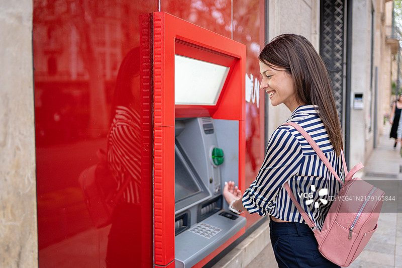 在西班牙马略卡岛帕尔马，年轻女子在街边的ATM机上用智能手表取款图片素材