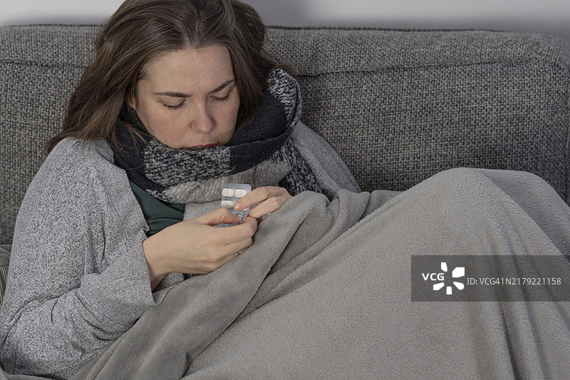 生病的女人盖着毯子在沙发上服用退烧药图片素材