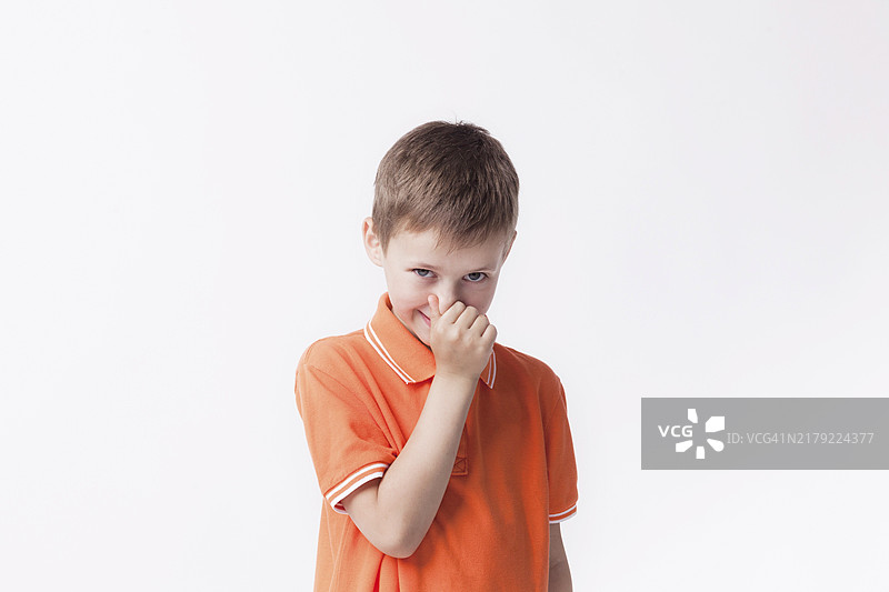 男孩用手指捏着鼻子，看着镜头，白色背景图片素材