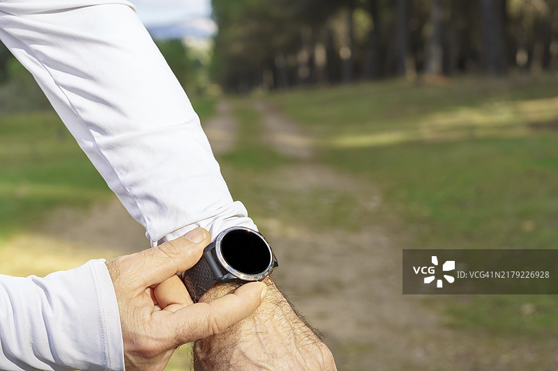 男子在田野里使用智能手表训练，背景是松树林图片素材