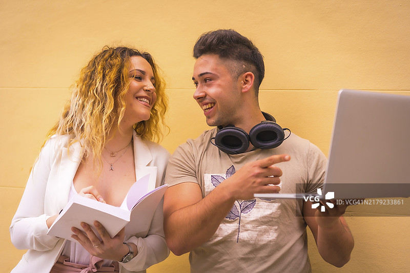 年轻创业情侣进行团队合作，背景为黄色，男孩戴着音乐耳机，女孩穿着白色西装，使用电脑图片素材