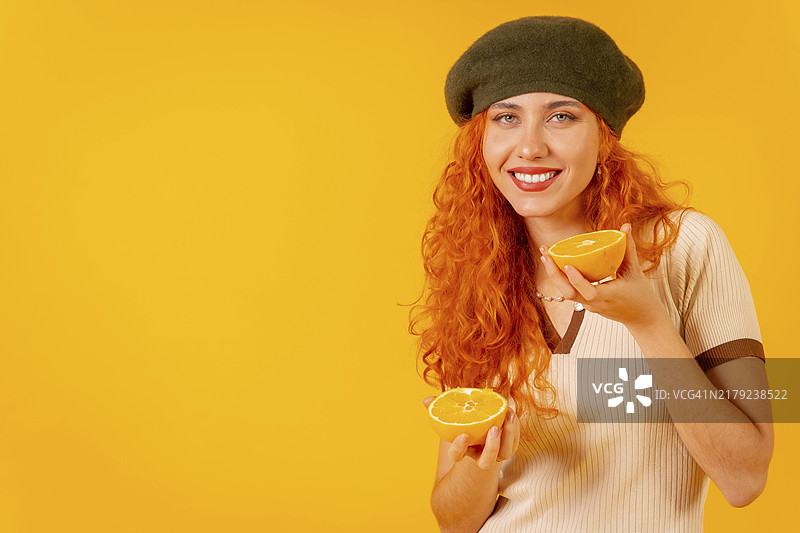 拿着橘子，在黄色背景下非常开心的红发女人图片素材