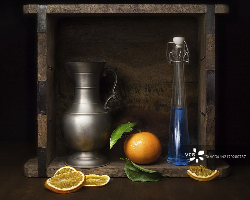 玻璃瓶、橘子和锡制水罐静物，工作室拍摄，深色背景图片素材