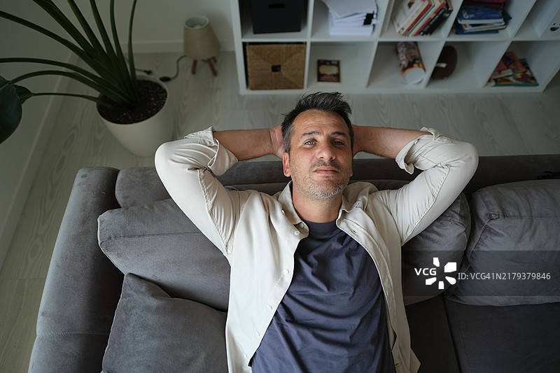 沉思的严肃男人坐在家里的沙发上，陷入沉思。图片素材