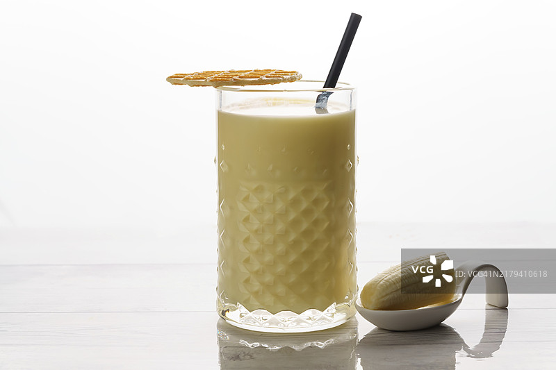 白色背景下含香蕉、饼干和吸管的香蕉奶昔特写图片素材