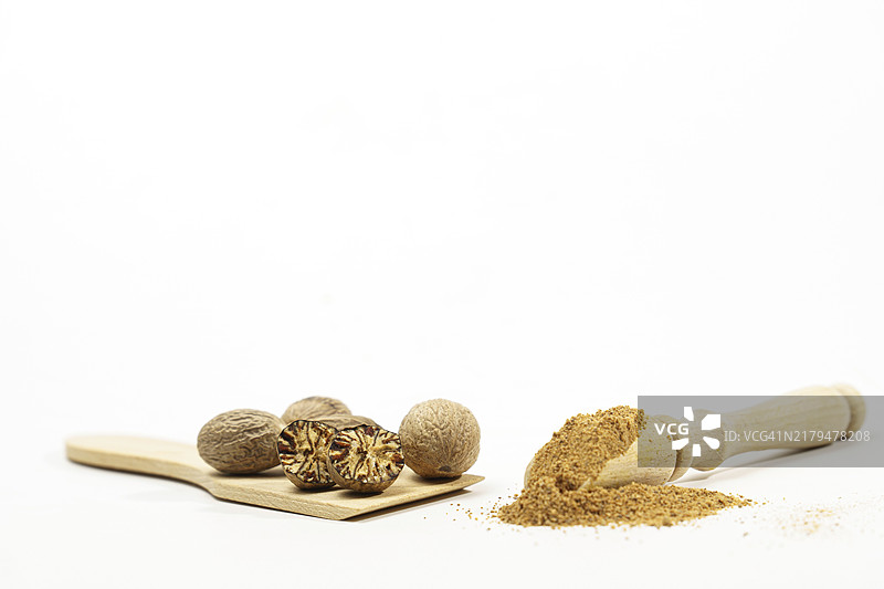 完整、对半切开并研磨的肉豆蔻，放在白色背景的木勺上，留有复制空间图片素材