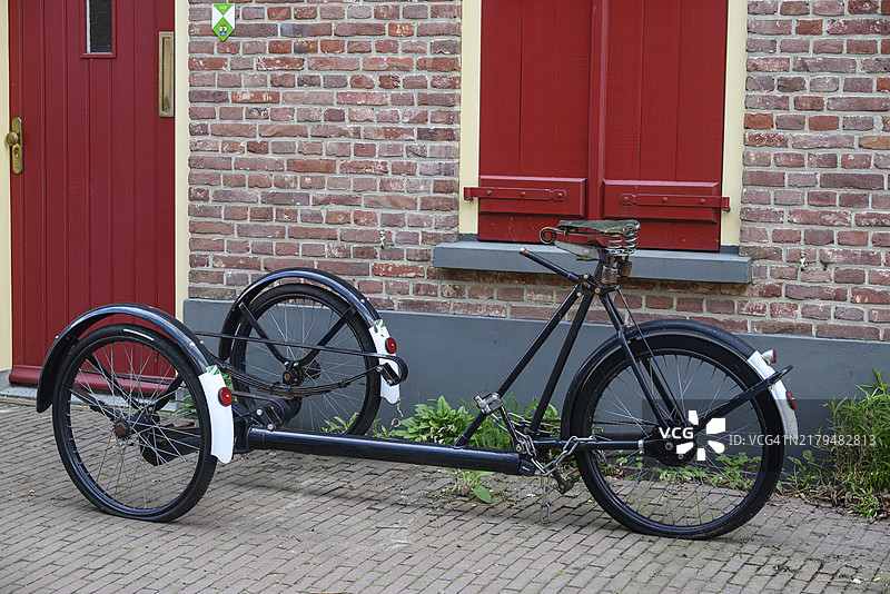 古董自行车拖车停在红门砖墙前，具有复古外观，位于荷兰海尔德兰省布雷德福特图片素材