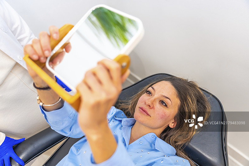 年长的白人妇女躺在美容院的担架上，照镜子后在嘴唇上涂抹玻尿酸图片素材