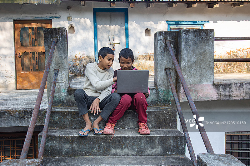 农村场景中在水泥楼梯上使用笔记本电脑的两个男孩图片素材