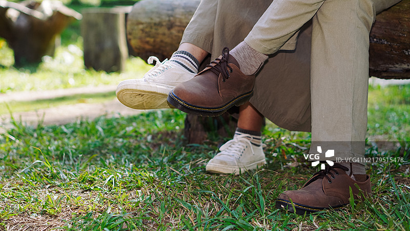 一对情侣穿着休闲鞋的腿悬挂在木椅上图片素材